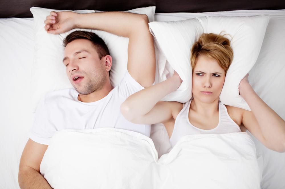 woman blocking ears with pillow while husband snores