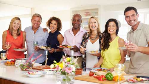 group of friends smiling around a kitchen island with food on it