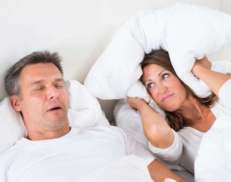 man snoring while wife holds a pillow over her ears