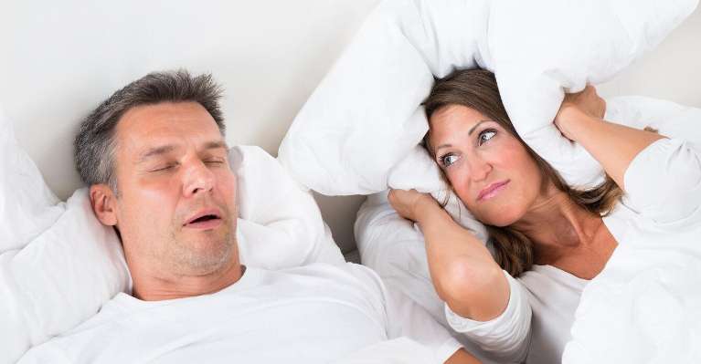 woman holding pillow over her ears while her husband snores next to her